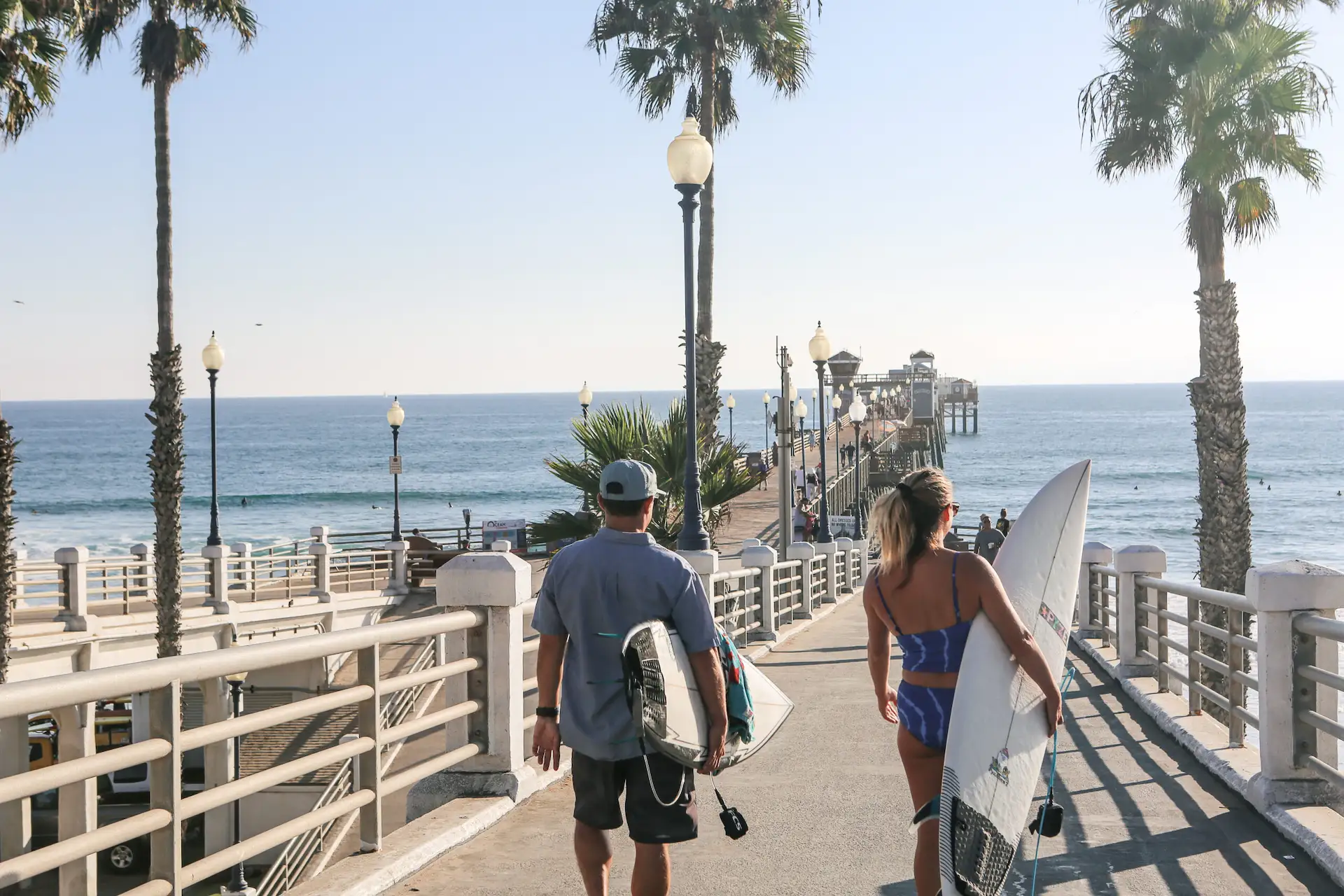 2 people walking down Oceanside Pier with surfboards