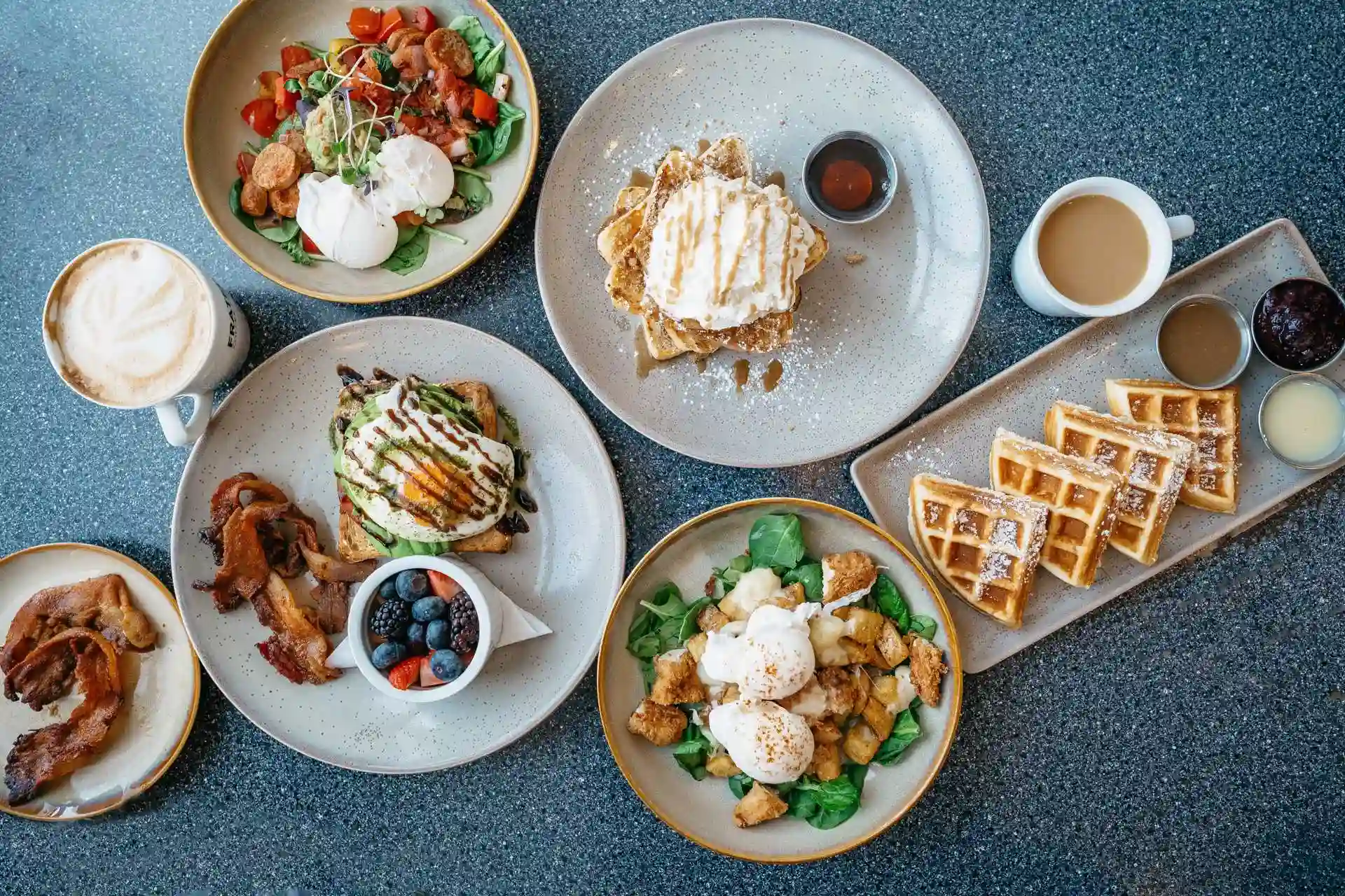 Brunch spread with poached eggs, avocado toast, waffles, berries, and cappuccino arranged on a cozy table for a vibrant mid-morning feast.