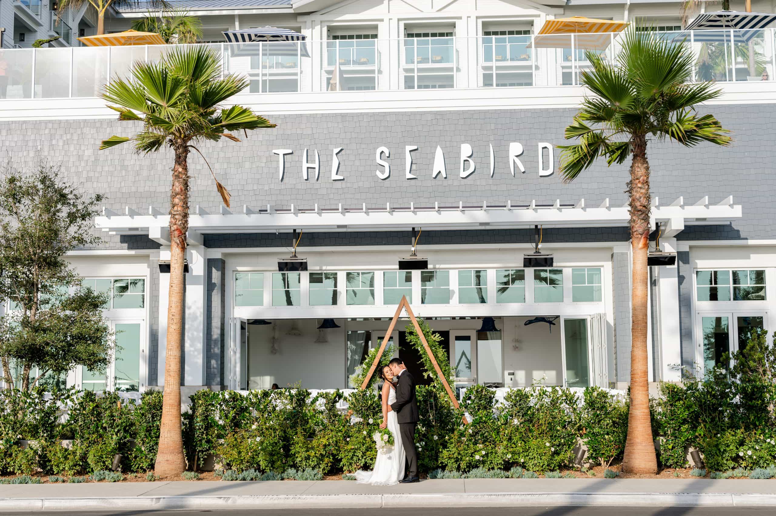 A married couple kissing in front of the Seabird facade