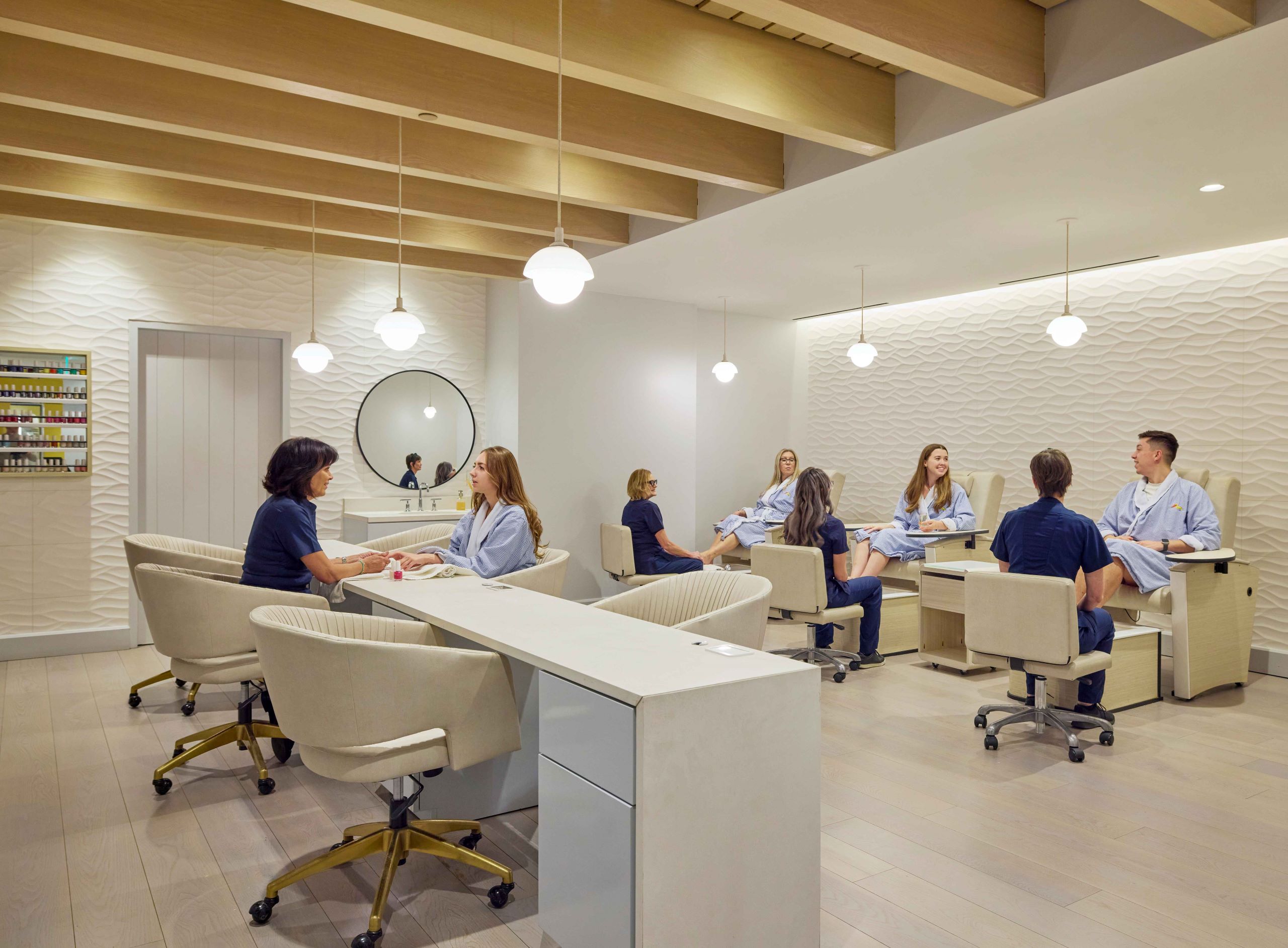 Modern nail salon with clients receiving manicures and pedicures, beige chairs, wood floors, and globe pendant lighting.