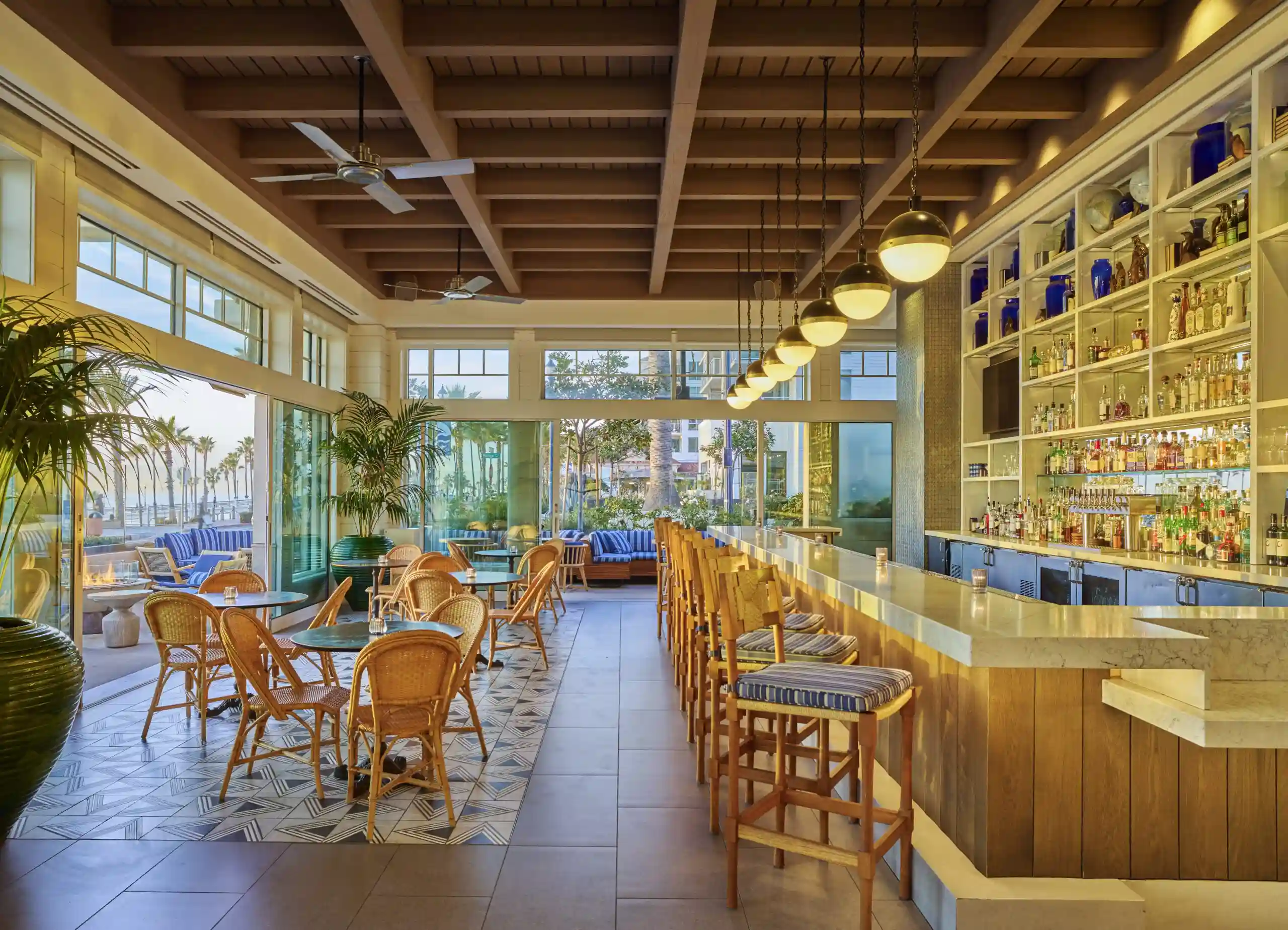 Stylish bar at The Seabird Resort with marble counters, wicker chairs, and coastal views through floor-to-ceiling windows.