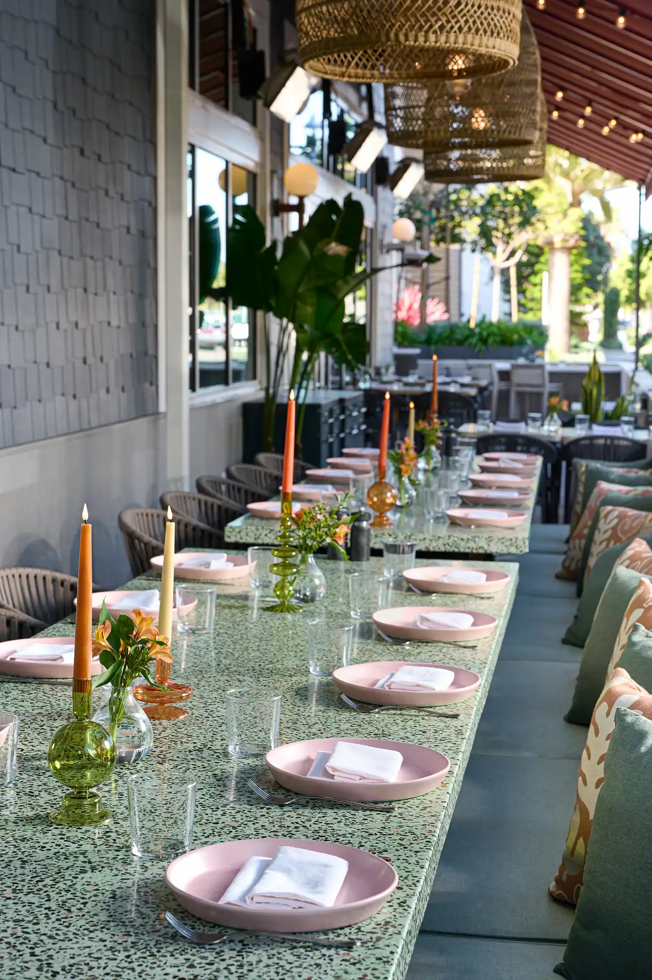Dining table with pink plates, orange flowers, and candles under wicker lights in stylish modern restaurant.